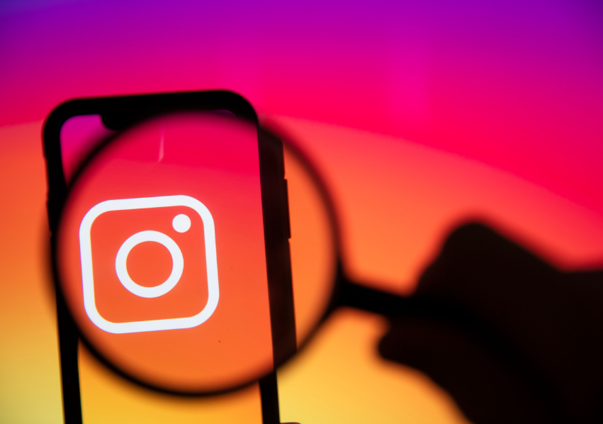 Comprar Seguidores: Como Funciona, Quais os Benefícios e os Perigos 4 Um smartphone com o logotipo do Instagram em sua tela é visto através de uma lupa, simbolizando a busca ou a análise cuidadosa da plataforma e dos serviços para comprar seguidores.