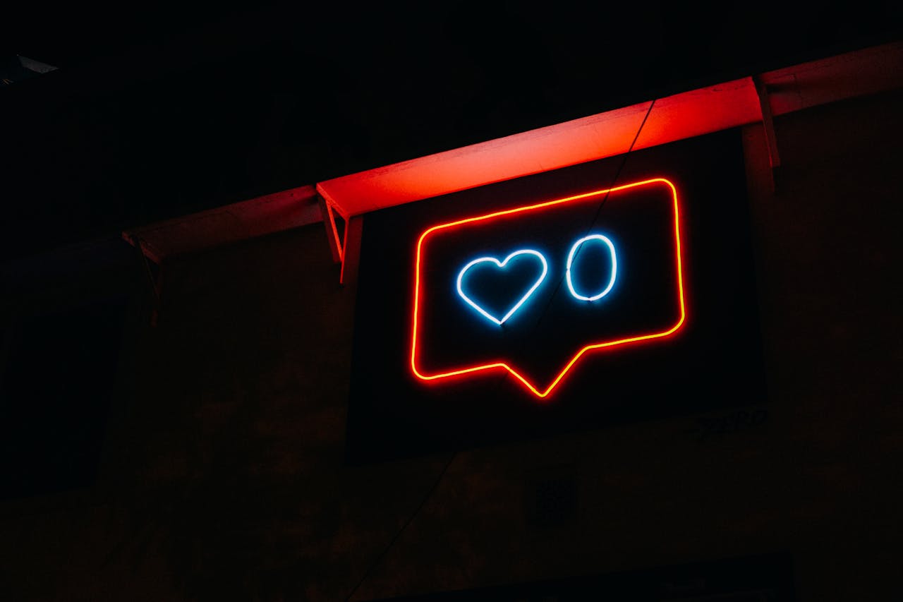 Comprar Seguidores: Como Funciona, Quais os Benefícios e os Perigos 3 Uma placa de neon brilhante em um ambiente escuro, exibindo um ícone de balão de mensagem com um coração azul no centro e um contorno vermelho, simbolizando o engajamento que se busca ao considerar a opção de comprar seguidores.