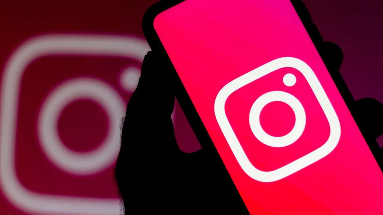 Por Que Baixar Stories do Instagram Pode Ser Fundamental? 7 Um smartphone é segurado por uma mão silhuetada, exibindo o vibrante logotipo do Instagram em sua tela rosa. Ao fundo, um segundo logotipo desfocado do Instagram é visível. A imagem representa o aplicativo do Instagram, onde os usuários podem visualizar e potencialmente baixar stories do Instagram.