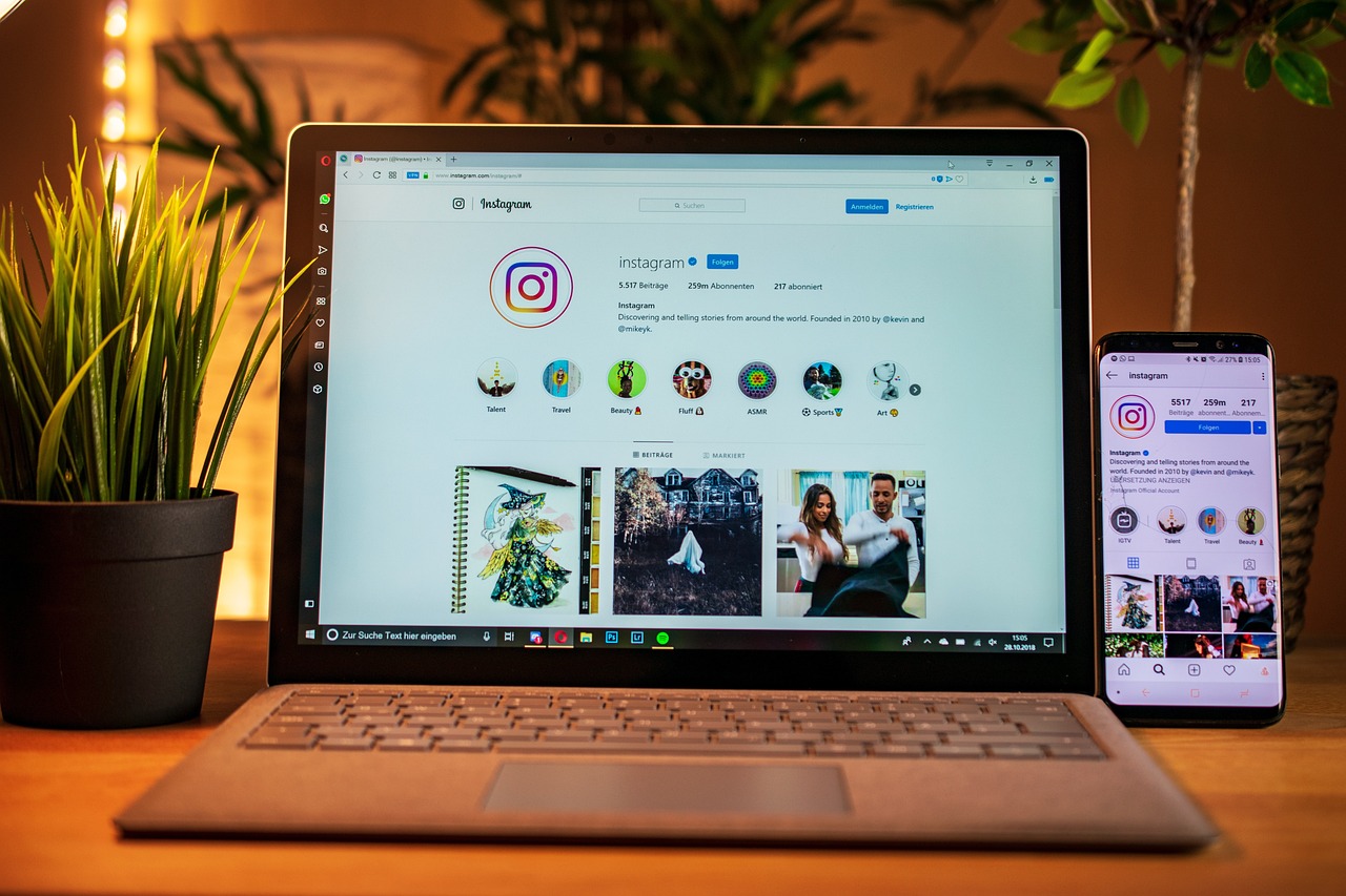 Legendas para Fotos: Frases Criativas e Inspiradoras para Instagram 2025 7 Um laptop exibe a página inicial do Instagram, com a interface do perfil visível. Ao lado, um smartphone também mostra o aplicativo do Instagram aberto. Uma planta verde em um vaso preto e outra planta menor completam a cena em uma mesa de madeira. A imagem sugere a gestão de conteúdo em redes sociais, criação de posts ou busca por inspiração em Legendas para Fotos.
