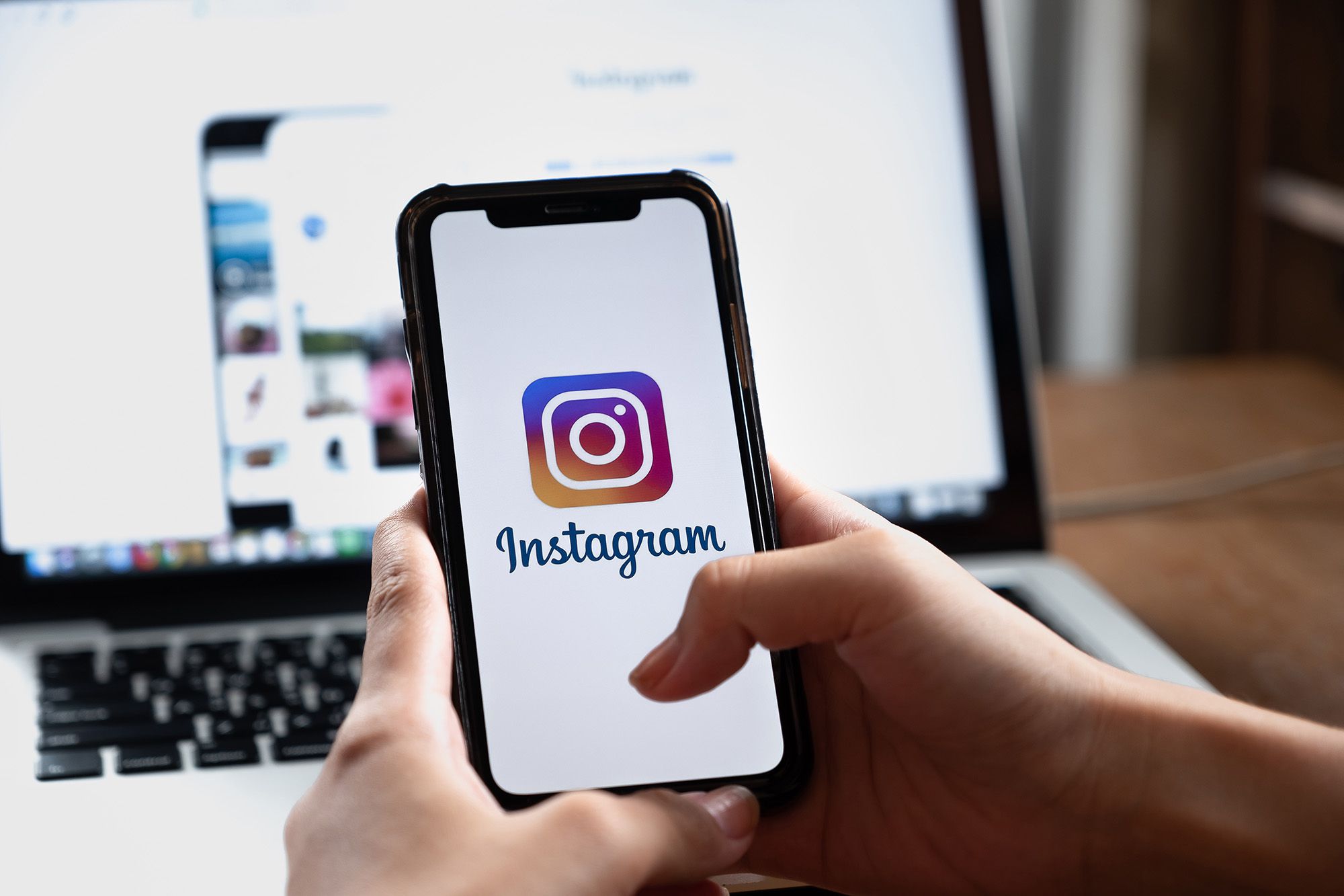 imagem de logo do instagram aberta no iphone com laptop de fundo, mostrando estratégia de instagram para ganhar seguidores e clientes
