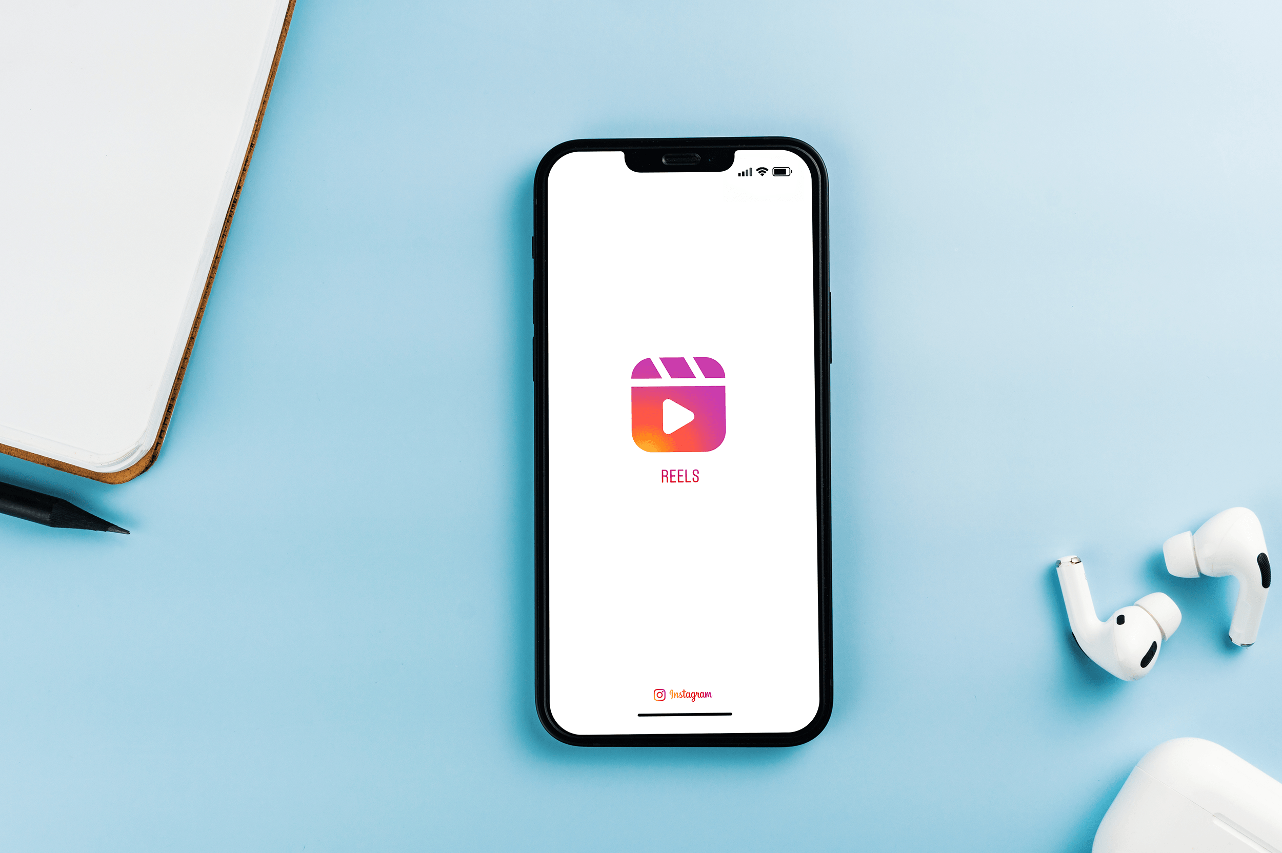 Tendências de Marketing Digital e o Impacto no Engajamento de Reels 1 iphone exibindo a tela inicial do Instagram Reels sobre uma mesa organizada, simbolizando o uso de vídeos curtos como estratégia eficaz de marketing digital para engajar o público nas redes sociais.