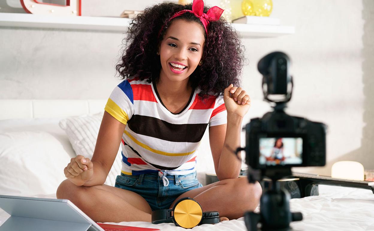 Mulher sentada na cama, sorrindo e gesticulando para uma câmera, com equipamentos de gravação próximos. Essa cena reflete a autenticidade e a conexão pessoal que os micro influenciadores estabelecem com seus seguidores ao criar conteúdo.