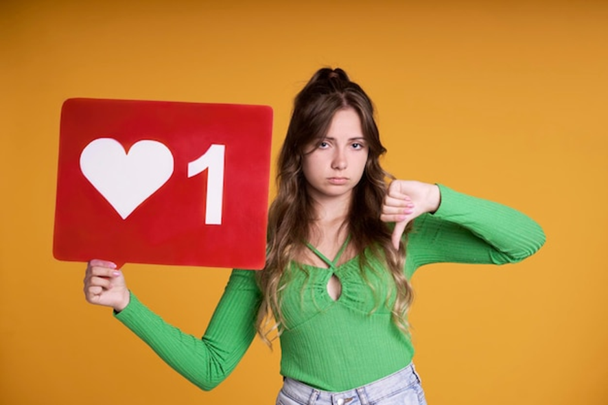 Uma jovem de blusa verde segura um cartaz vermelho com um ícone de coração e o número "1", demonstrando insatisfação ao dar um sinal de negativo com a outra mão. A cena contrasta com o desejo de alcançar 10 mil seguidores no Instagram, mostrando a frustração de ter pouca interação na plataforma.