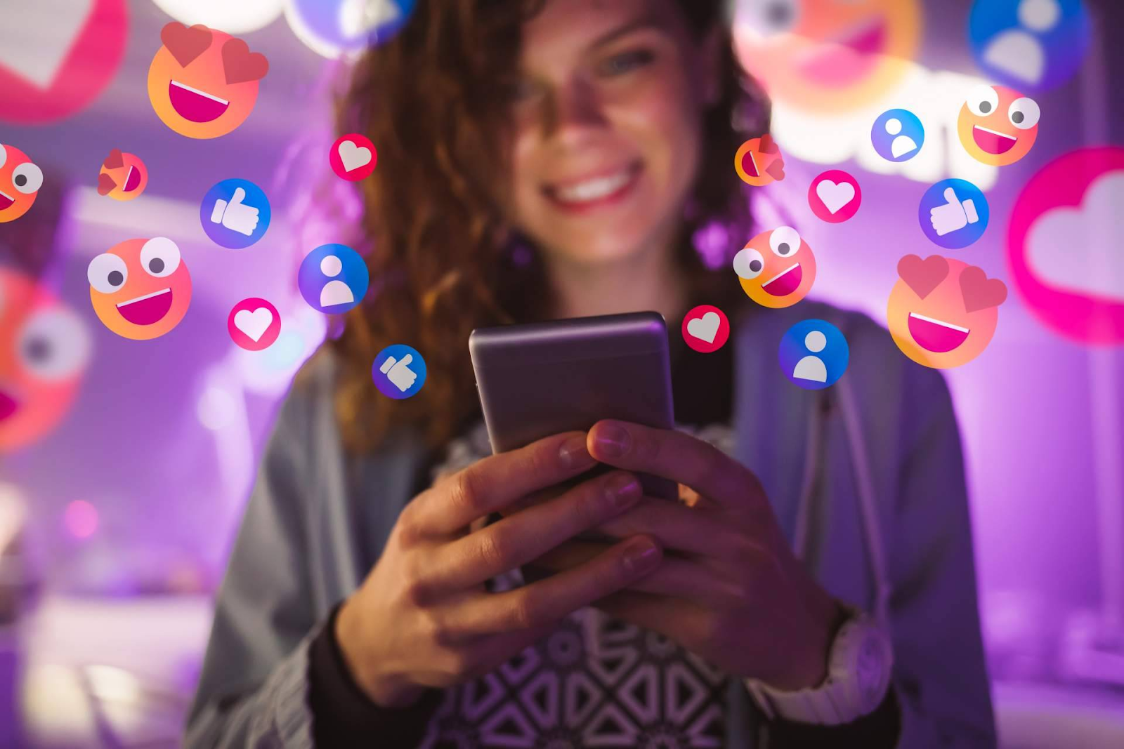 Uma mulher sorrindo enquanto interage com seu smartphone, cercada por ícones coloridos de reações e interações digitais, como corações e emojis. Esse cenário pode ser relacionado à compra de seguidores, uma estratégia comum para aumentar o engajamento e visibilidade nas redes sociais.