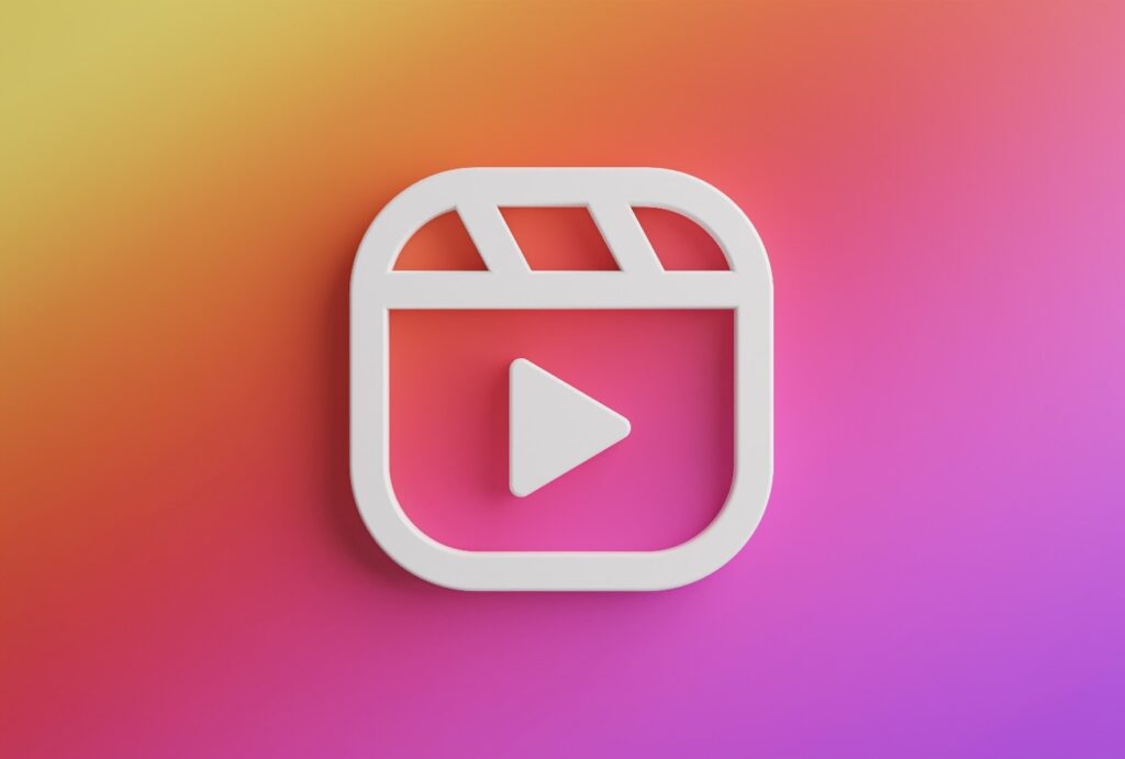 Reels para Empresas: Descubra Como Transformar Vídeos Curtos em Resultados Reais 1 O ícone do Reels para empresas, em um formato 3D branco e com um botão de "play", está no centro de um fundo com um gradiente de cores que variam de laranja para roxo.