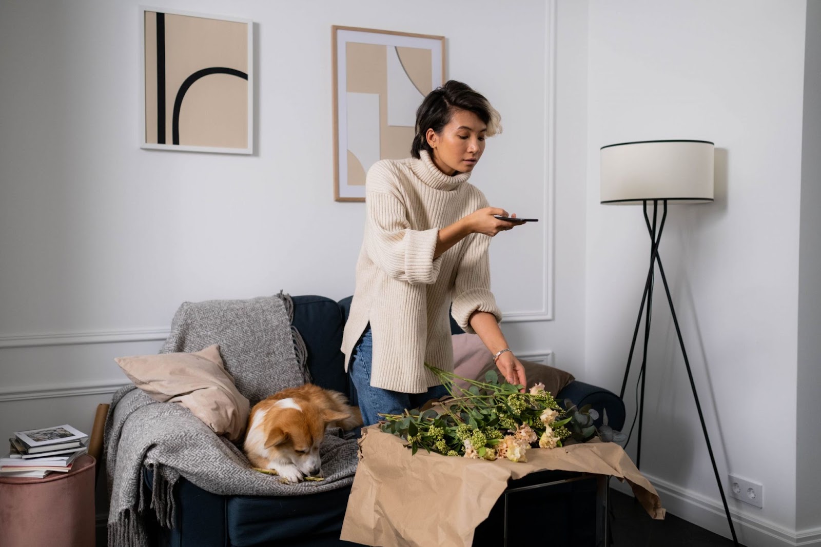 Reels para Empresas: Descubra Como Transformar Vídeos Curtos em Resultados Reais 4 Uma mulher em um ambiente interno moderno e iluminado está tirando fotos de um buquê de flores usando o celular. Há um cachorro dormindo no sofá ao lado. A cena ilustra a criação de conteúdo orgânico e autêntico para Reels para empresas.